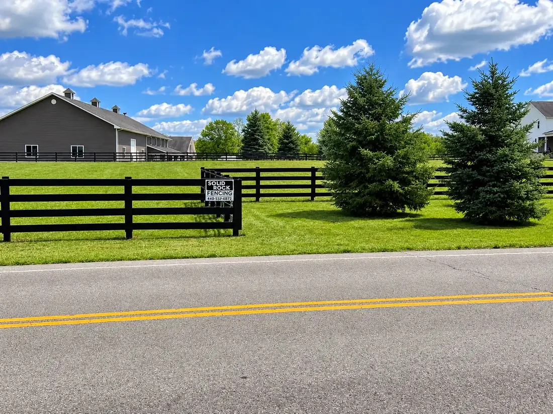 Black four-board fence and gate along a country road
